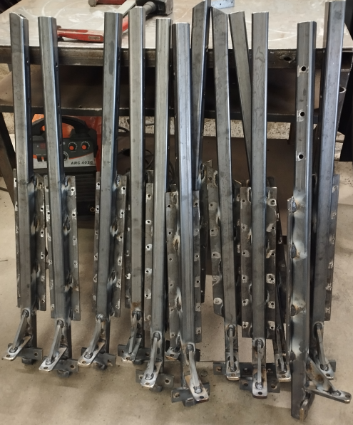 Les 12 premiers poteaux en cours de soudure. Les corps ont été assemblés aux pieds d'ancrage et aux "ailes" censées accueillir des panneaux de bois pour le remplissage. NB: Les 3 trous de 12 mm prévus pour laisser courir des câbles INOX.